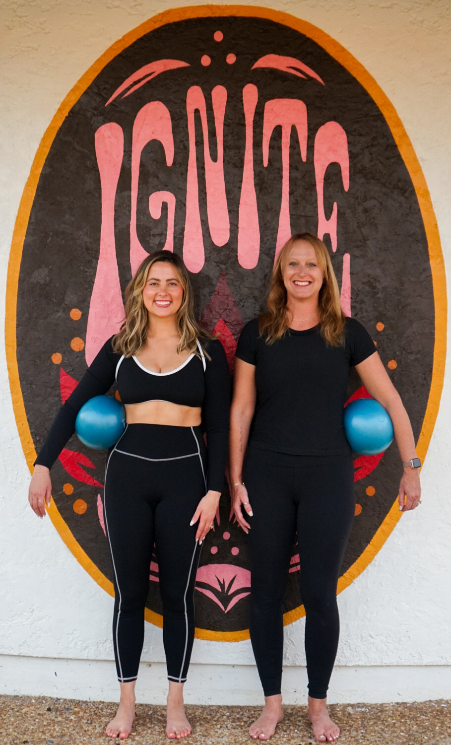 Two members of the Ignite community standing in front of the hand-painted studio mural